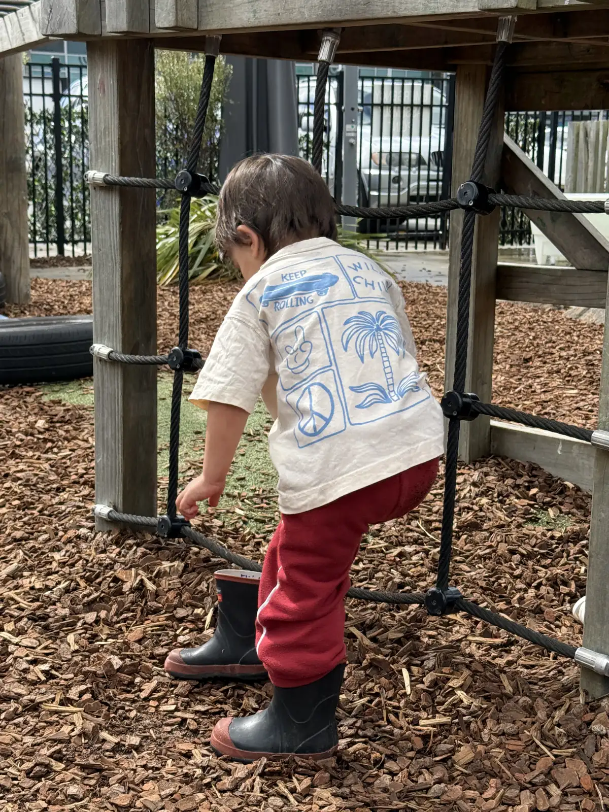 A child climbing up through the rope net underneath the timber fort.