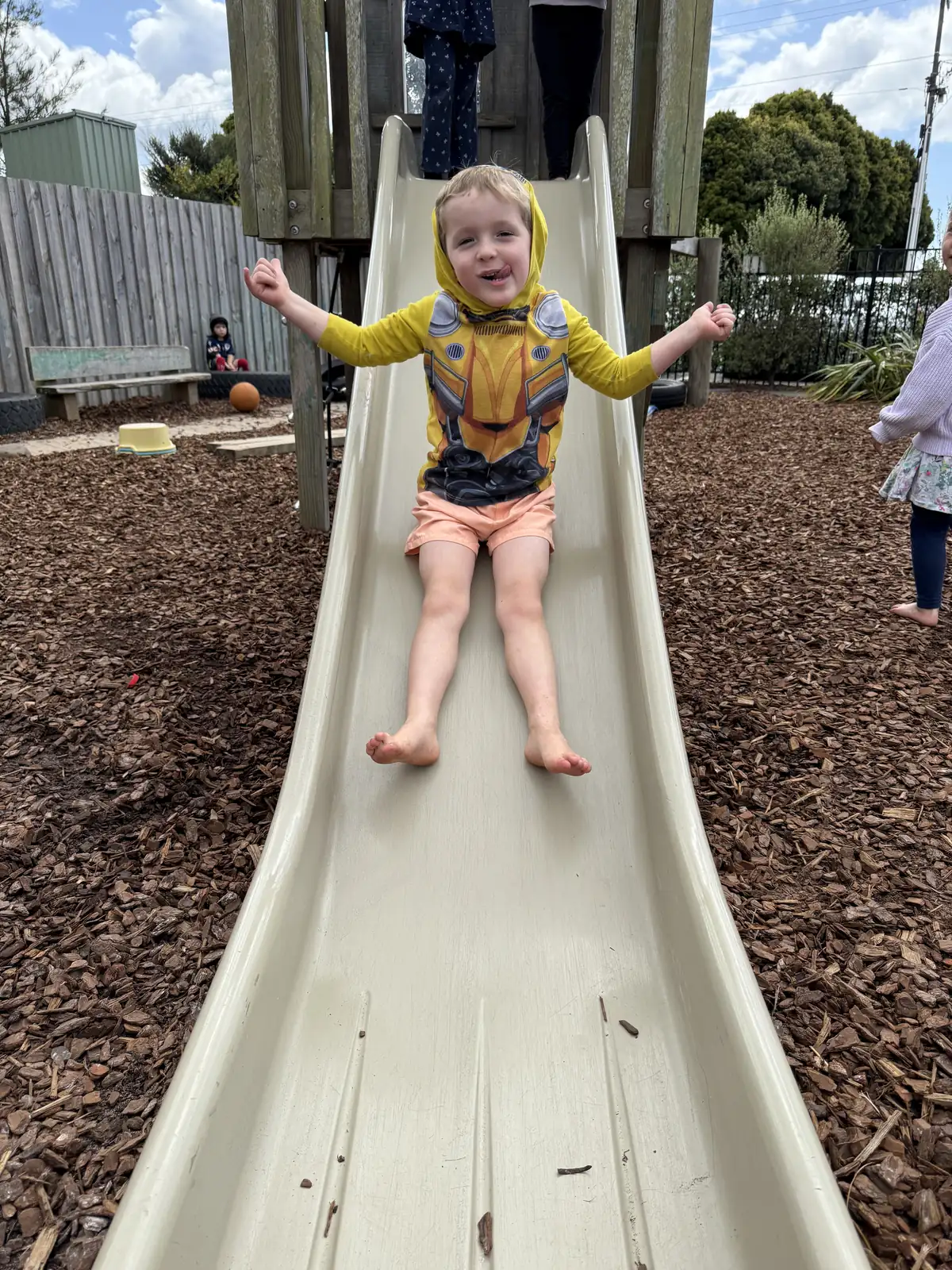 A child coming down the slide with both arms flung out, laughing.