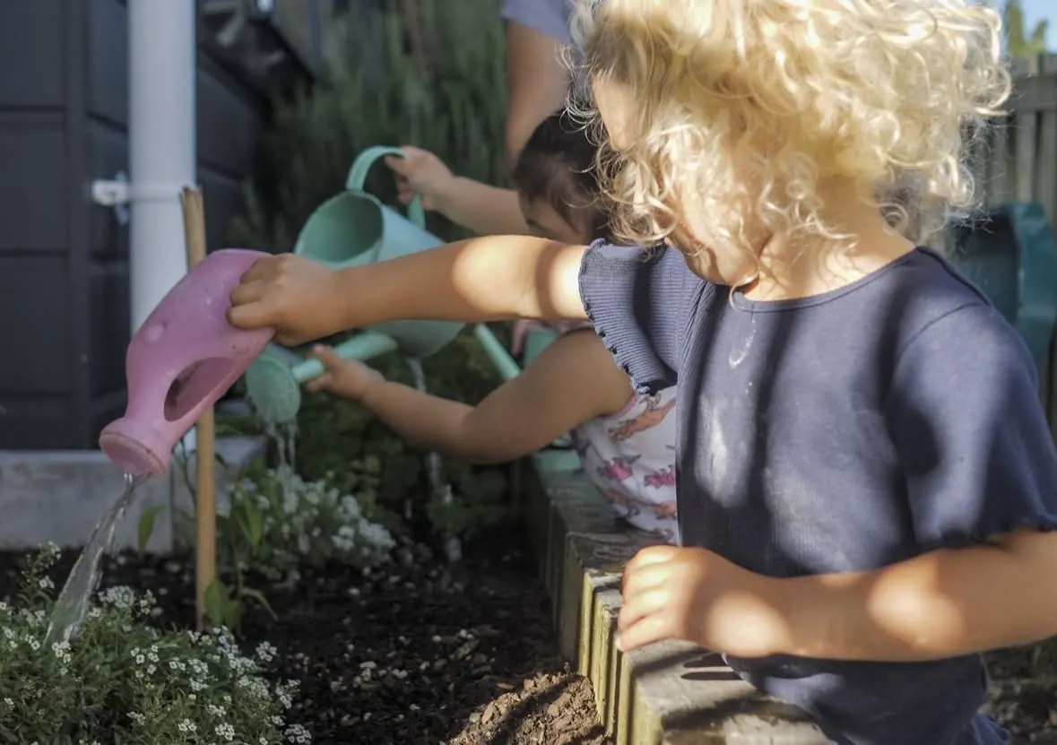 Two children watering the garden beds with watering cans.